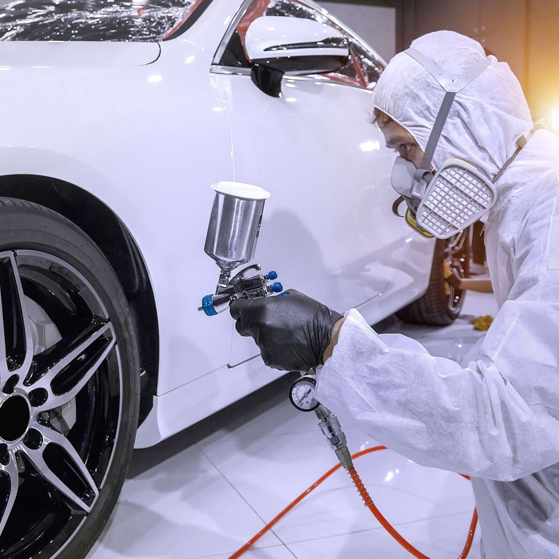 A man in a protective suit is spray painting a white car.