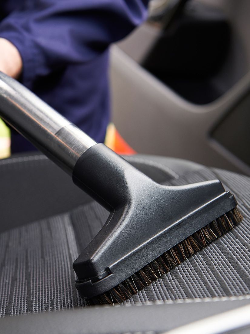 A person is cleaning a car seat with a vacuum cleaner.