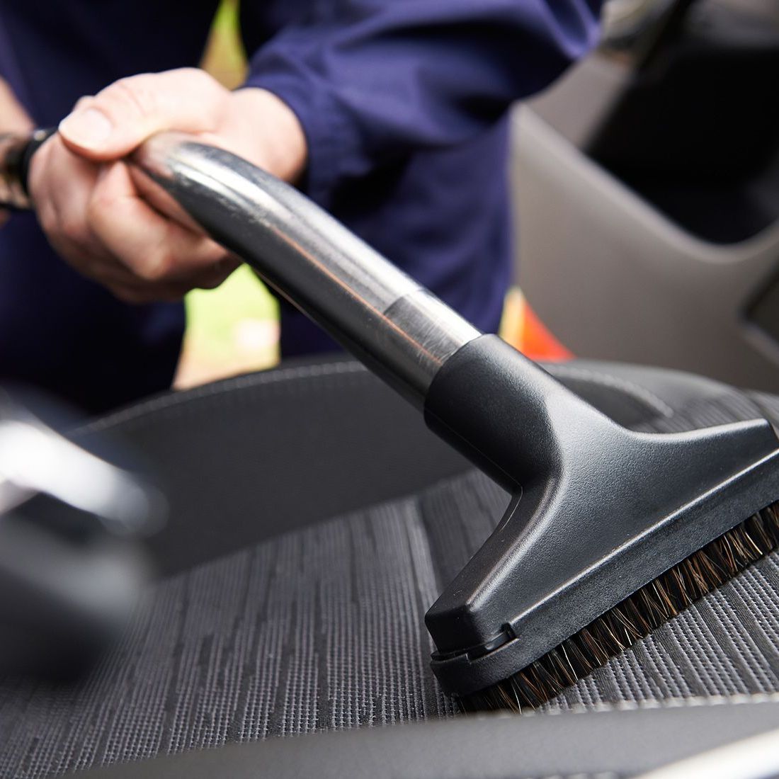 A person is cleaning a car seat with a vacuum cleaner