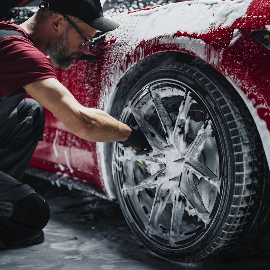 A man is cleaning the wheels of a red car with foam.