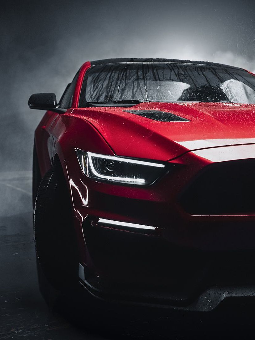A red sports car is parked on the side of the road in the rain.