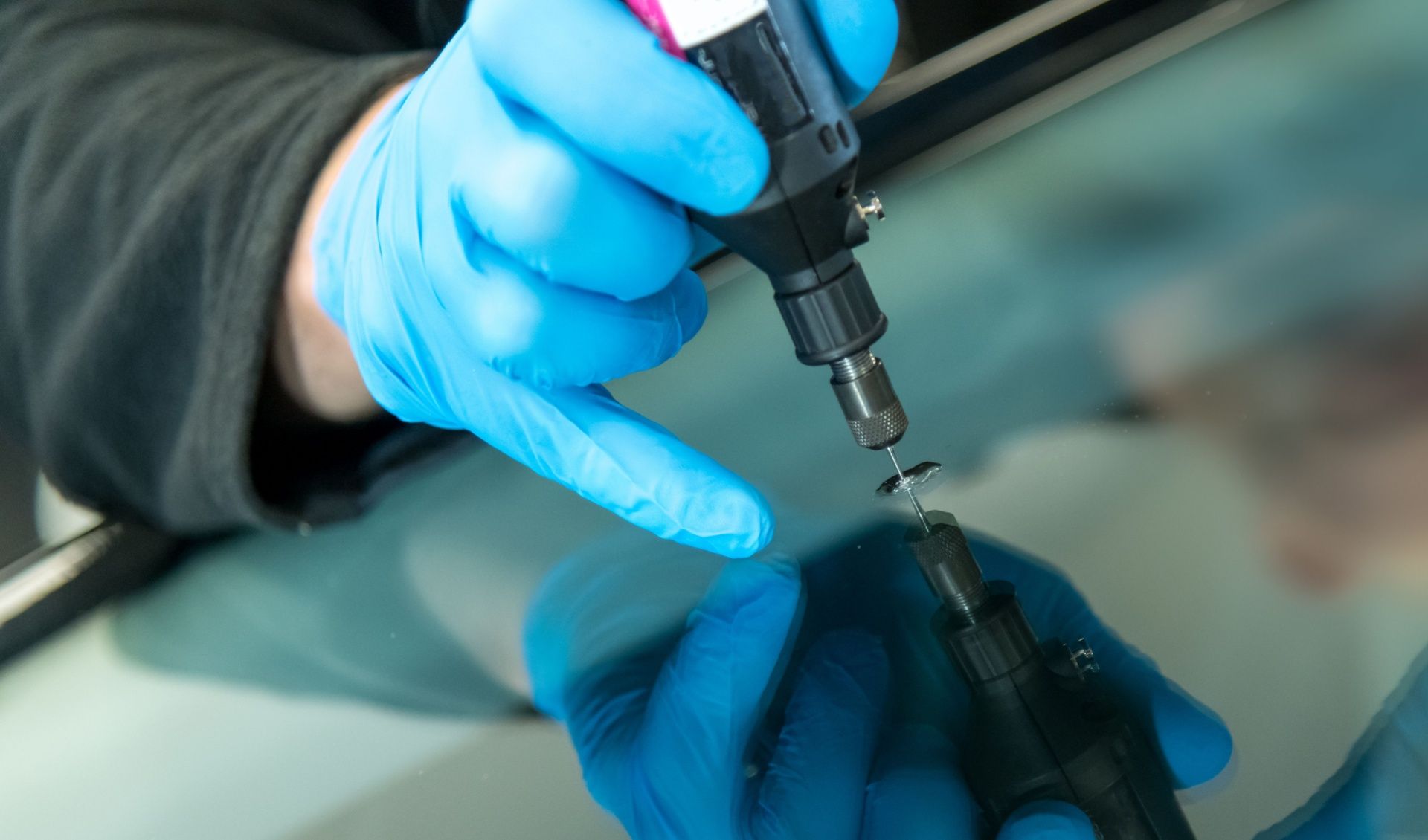 Gloved hands using a small tool to repair a cracked glass surface