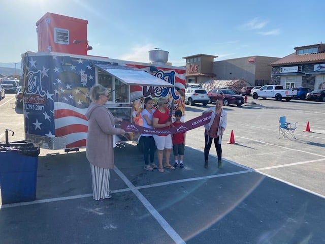 A group of people are standing in front of a food truck in a parking lot.
