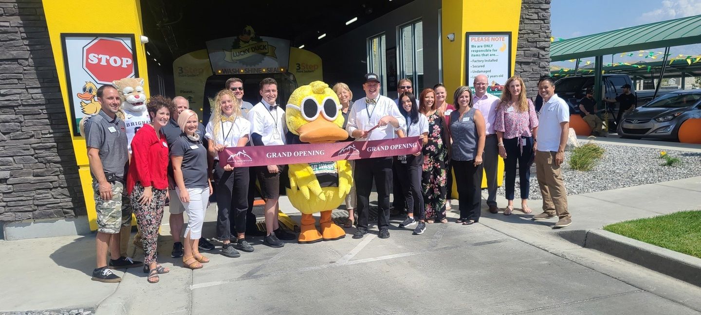 A group of people are standing in front of a yellow building holding a ribbon.