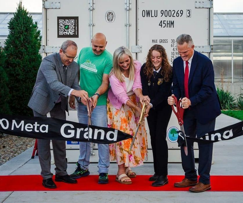 A group of people are cutting a black ribbon that says meta grand