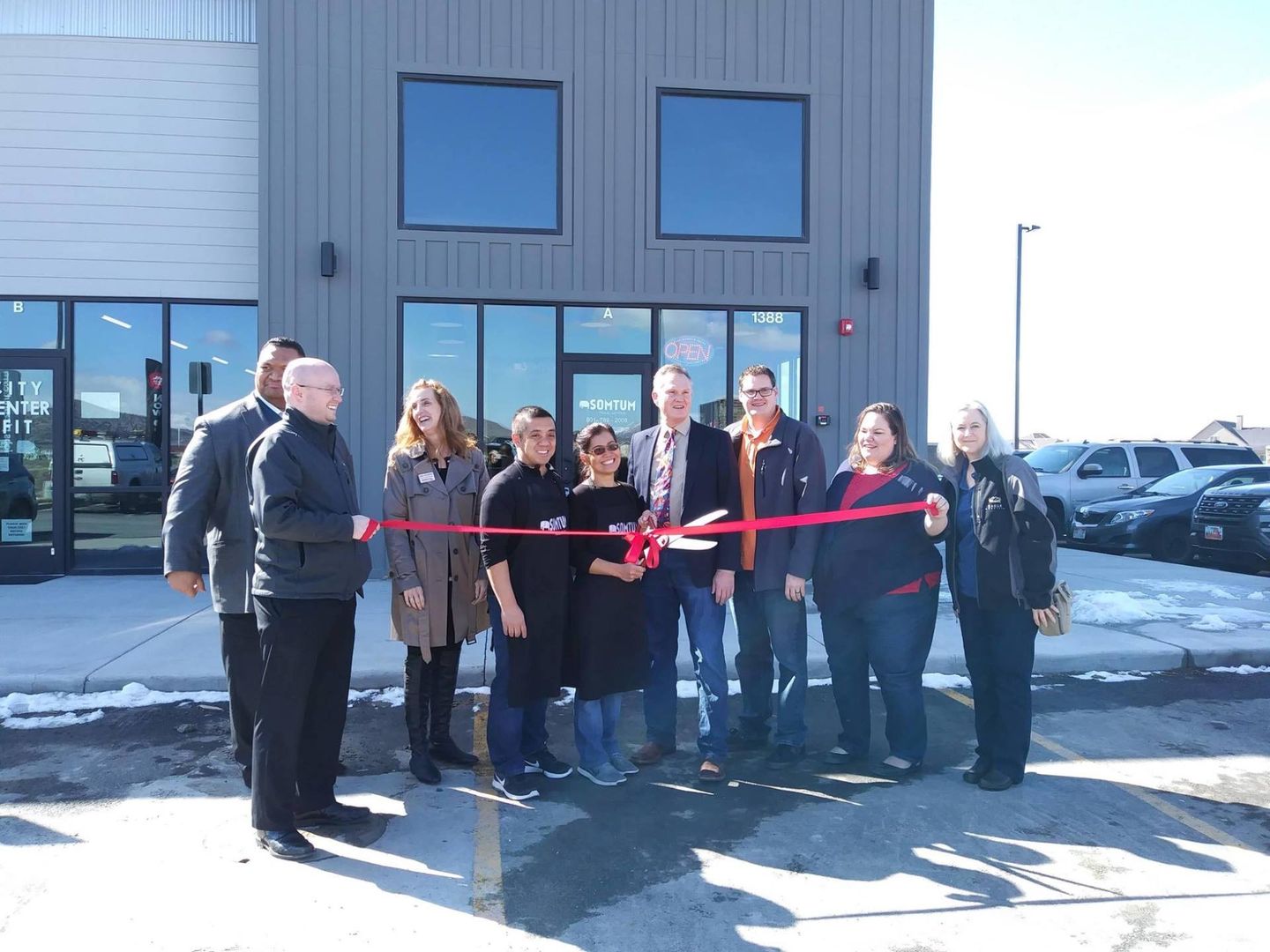 A group of people are cutting a red ribbon in front of a building.