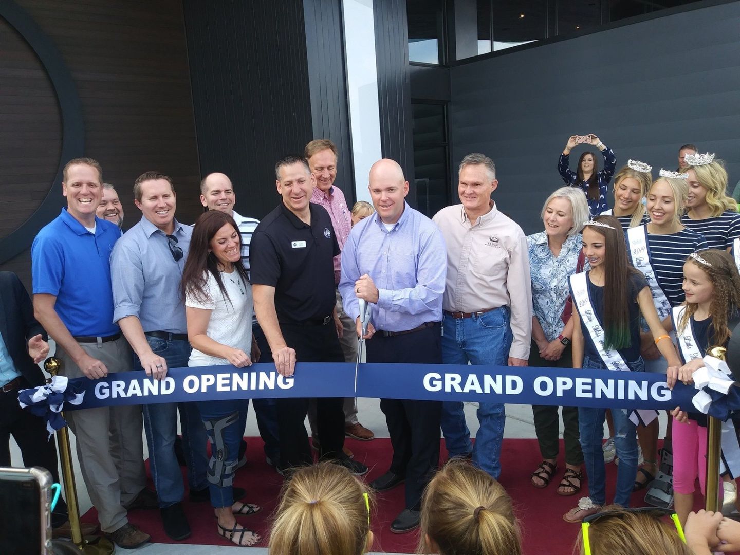 A group of people standing around a ribbon that says grand opening