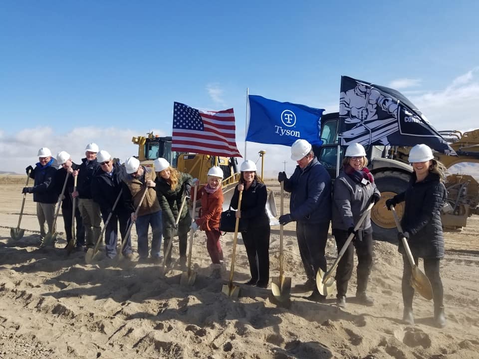 A group of people are standing in the sand with shovels and flags.