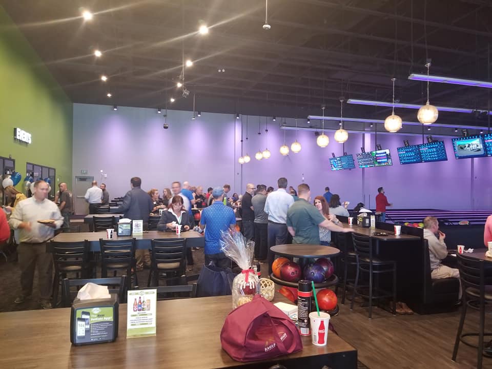 A group of people are sitting at tables in a bowling alley.