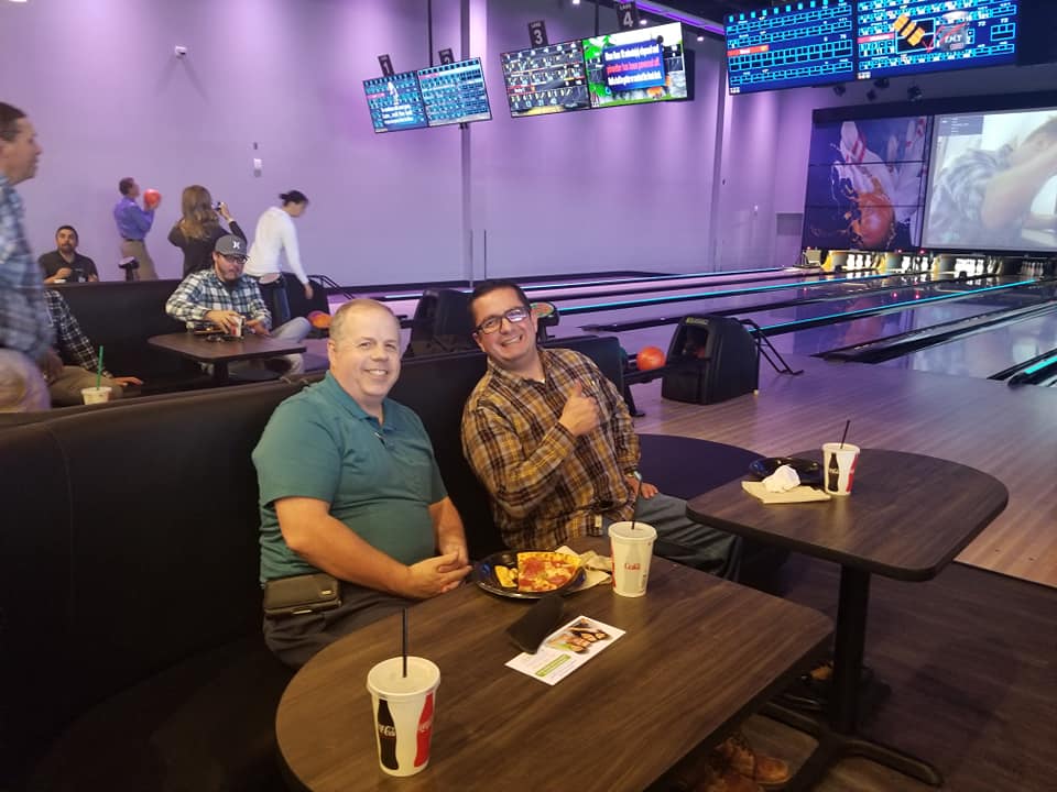Two men are sitting at tables in a bowling alley.