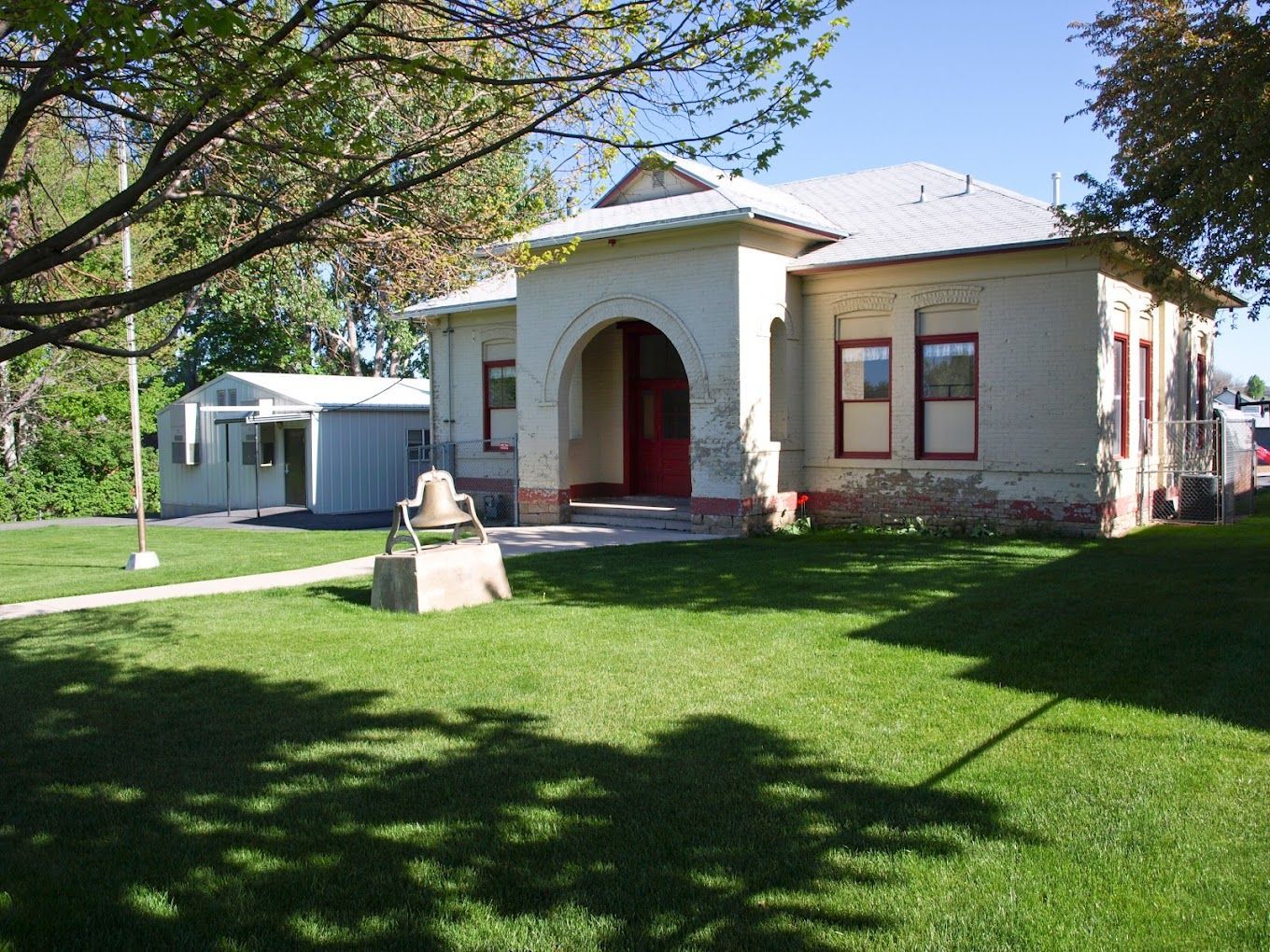 A large white building with a red door sits in the middle of a lush green field.