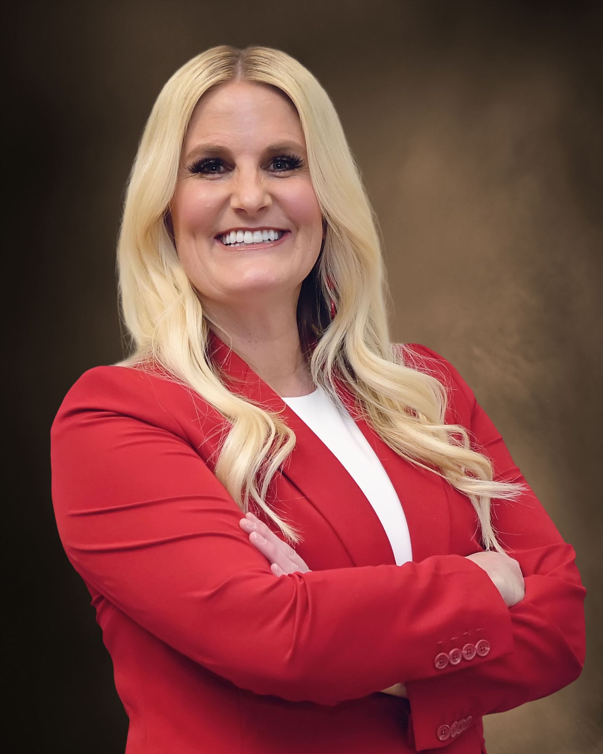 A woman in a red jacket is smiling with her arms crossed.