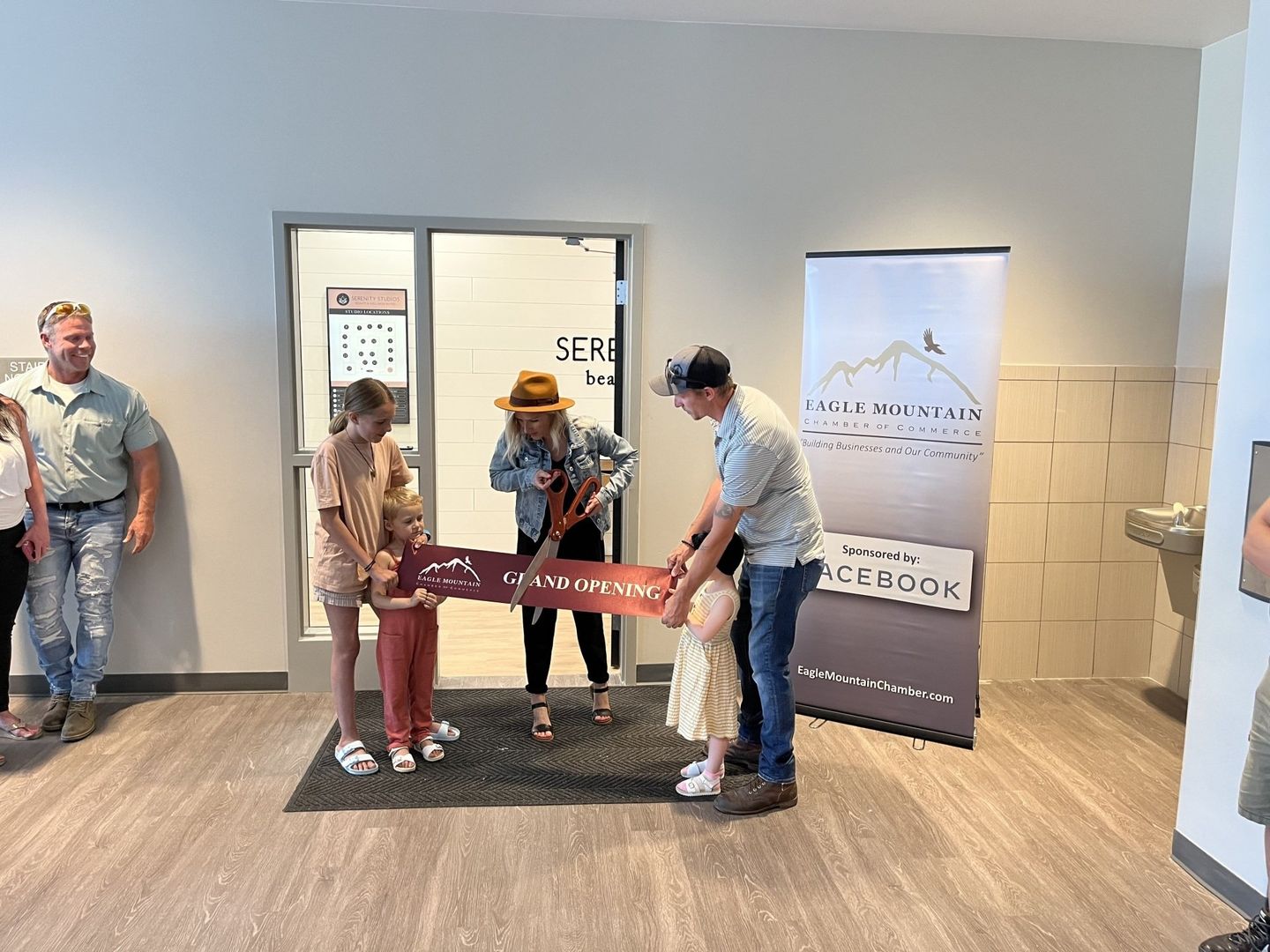 A group of people are standing in a room cutting a red ribbon.