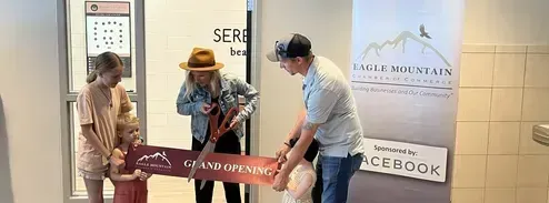 A group of people are cutting a red ribbon in front of a building.