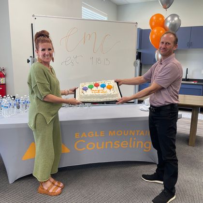 A man and a woman are holding a cake in front of a table that says eagle mountain counseling