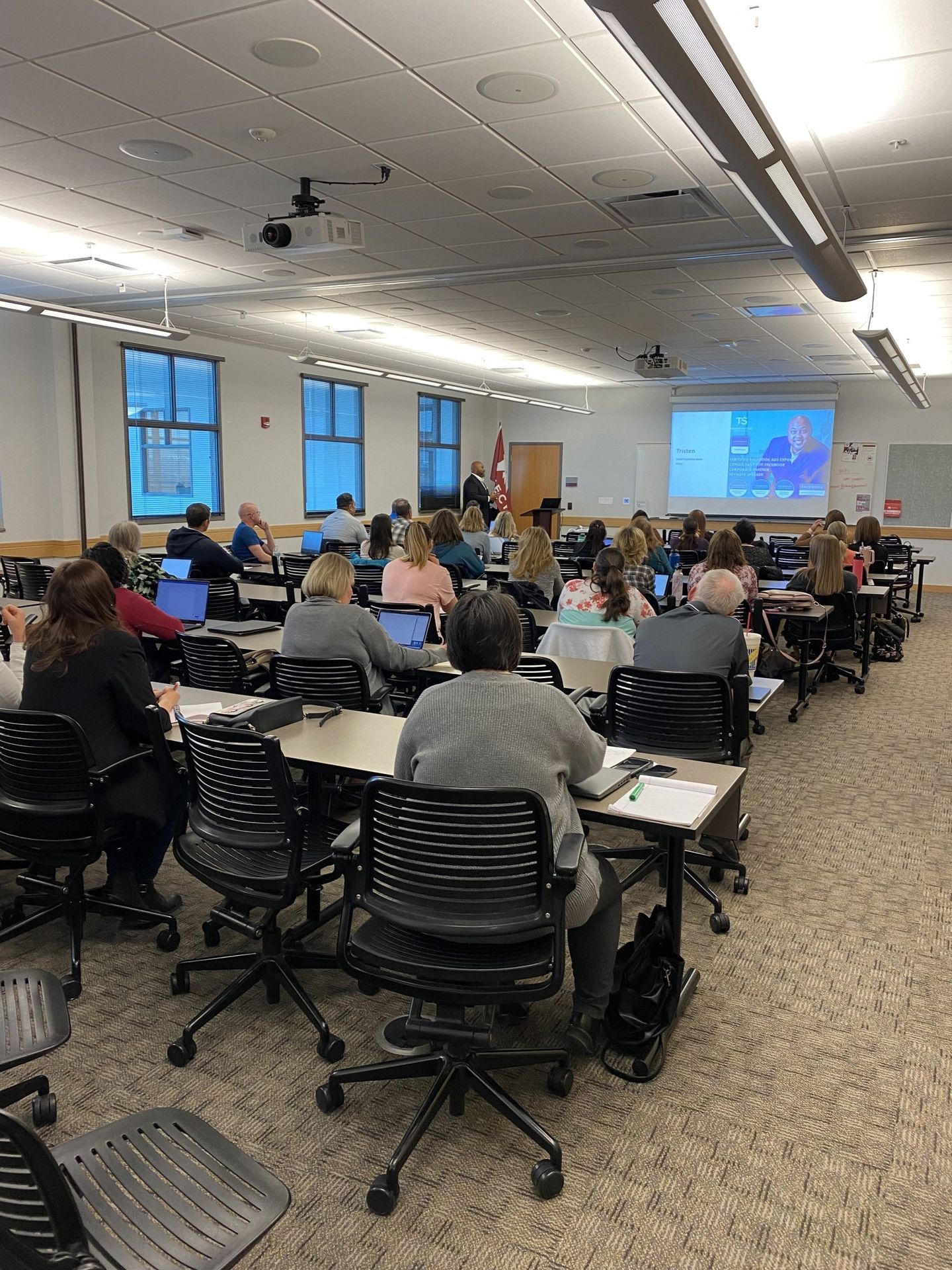 A large classroom filled with people sitting at desks and chairs.