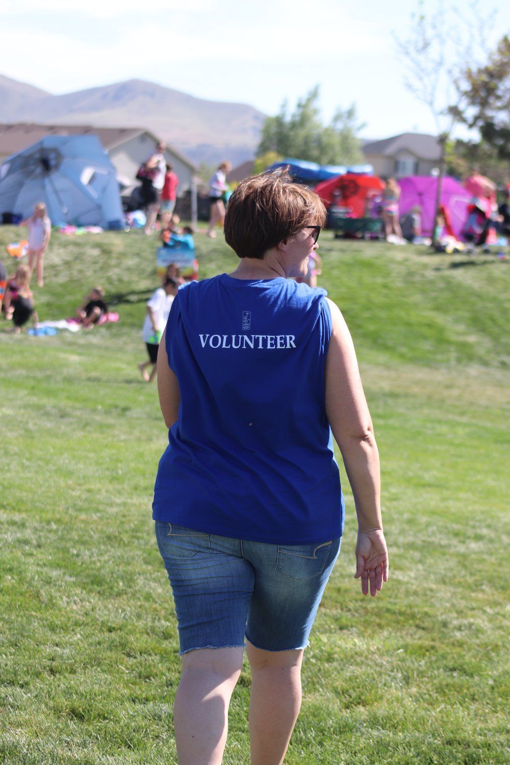 A woman wearing a blue volunteer shirt is walking through a grassy field.