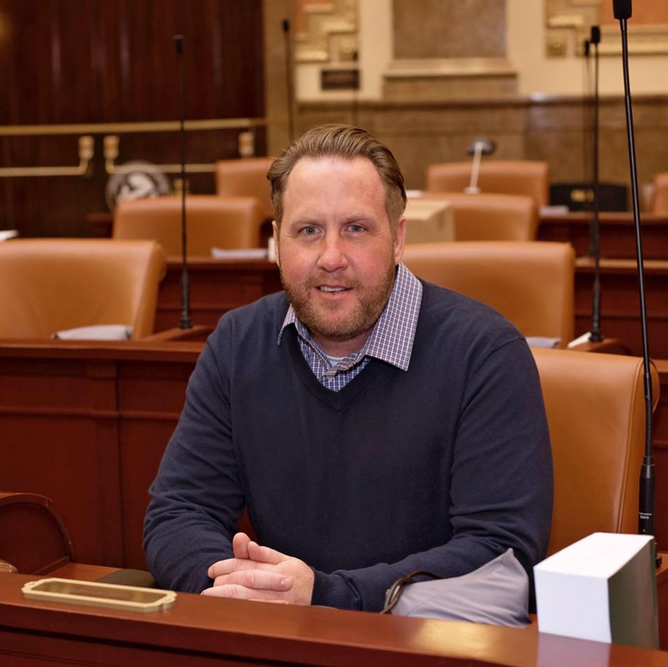 A man in a blue sweater is sitting at a desk in a conference room