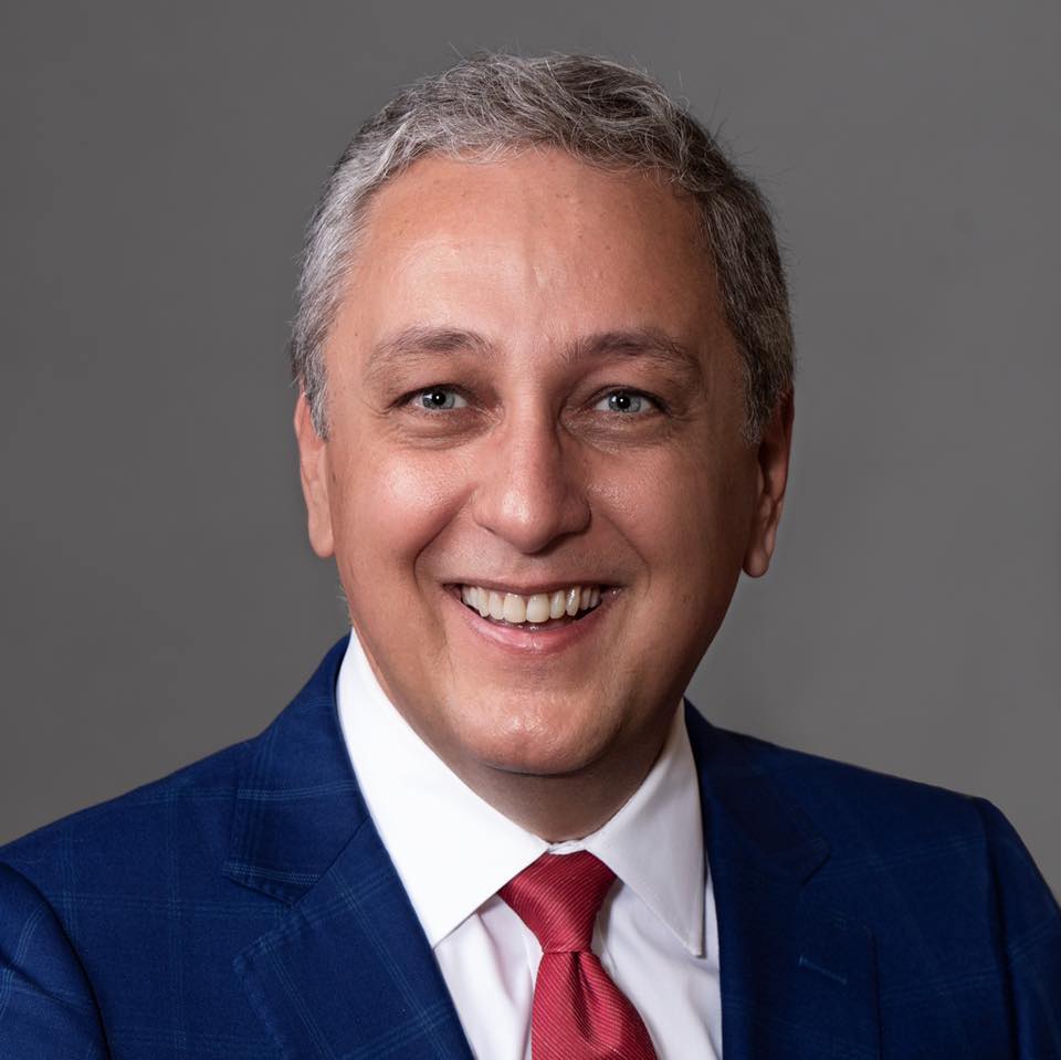 A man in a blue suit and red tie is smiling for the camera.