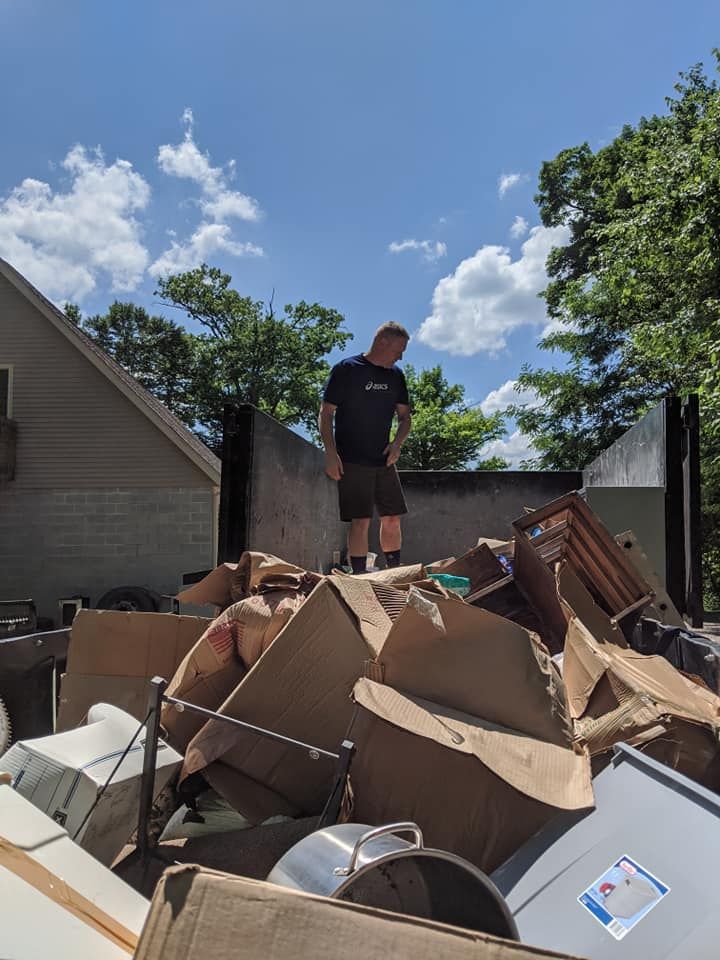 Man stands on pile of debris in front of a partially burned building on a sunny day.