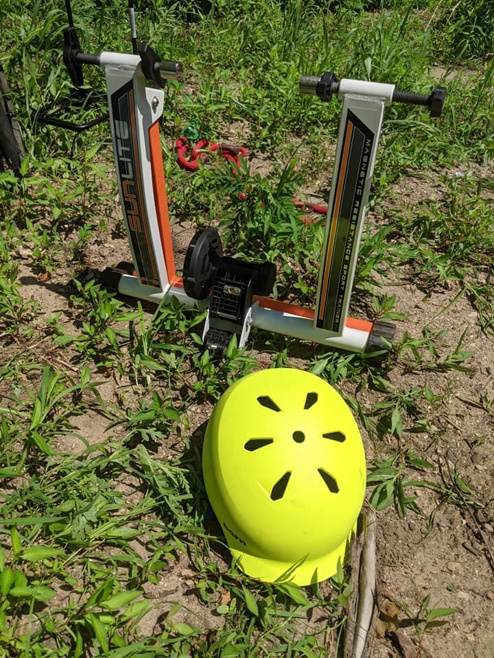 Cycling trainer and yellow helmet on the ground. Trainer is orange, black, and white.