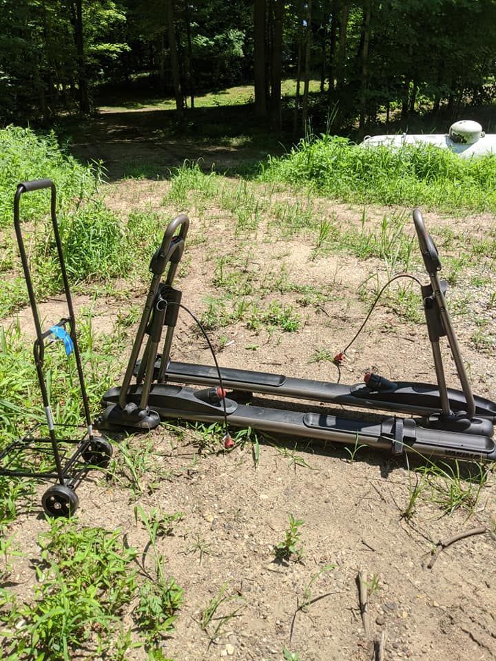 A black bike rack and cart sit on the ground outdoors, in front of greenery and trees.