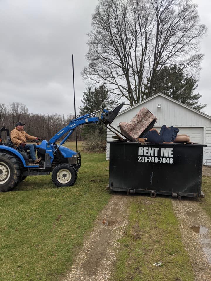 Man in tractor loading furniture into a black dumpster with 