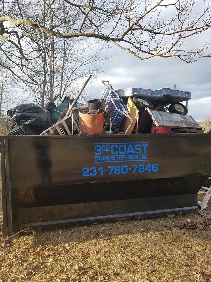 Black dumpster filled with trash outdoors, 3rd Coast Dumpster Rental logo visible.