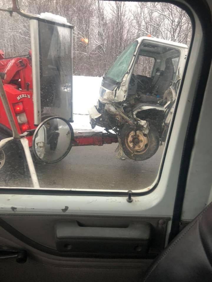 A damaged white truck being towed by a red tow truck on a snowy road.