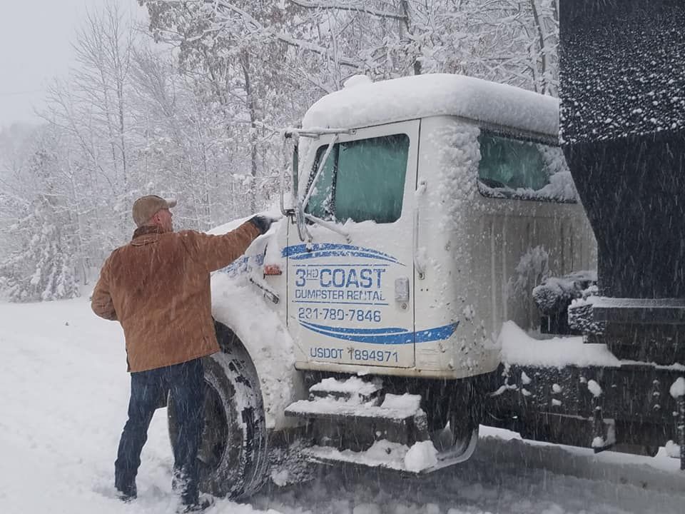 Man pointing at snowy truck, likely for snow removal. White truck, brown jacket, snow-covered setting.
