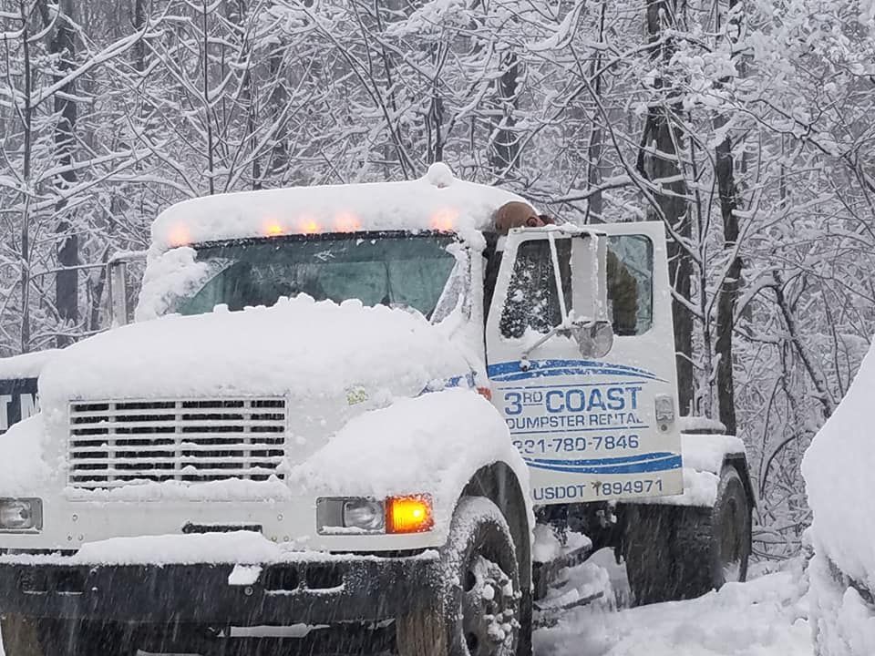 Snow-covered work truck with open door in a snowy forest; 3rd Coast Construction logo on door.