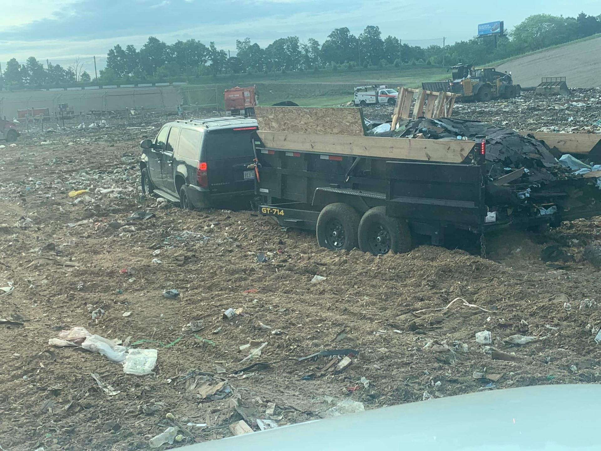 SUV towing a dump trailer stuck in mud at a landfill.