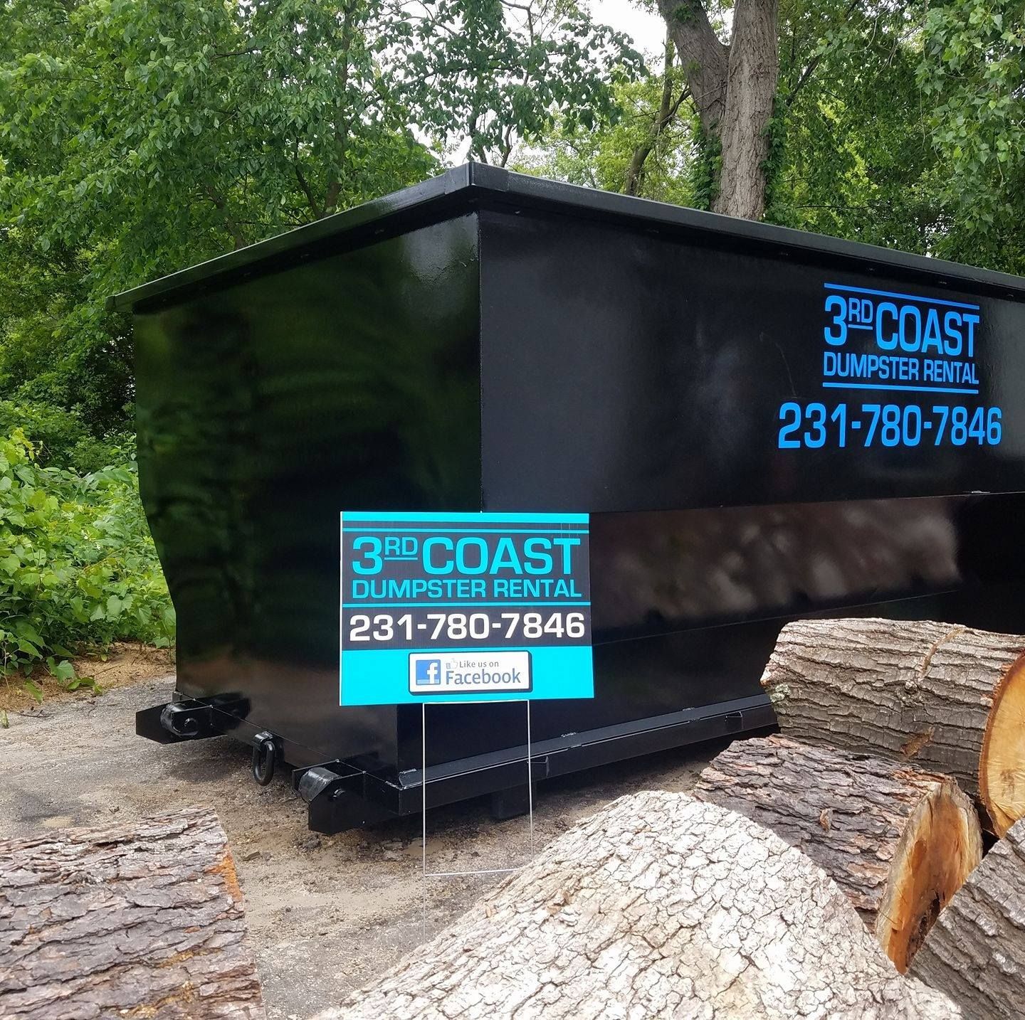 Black 3rd Coast dumpster rental. 231-780-7846 number. Sign in front of wood logs.