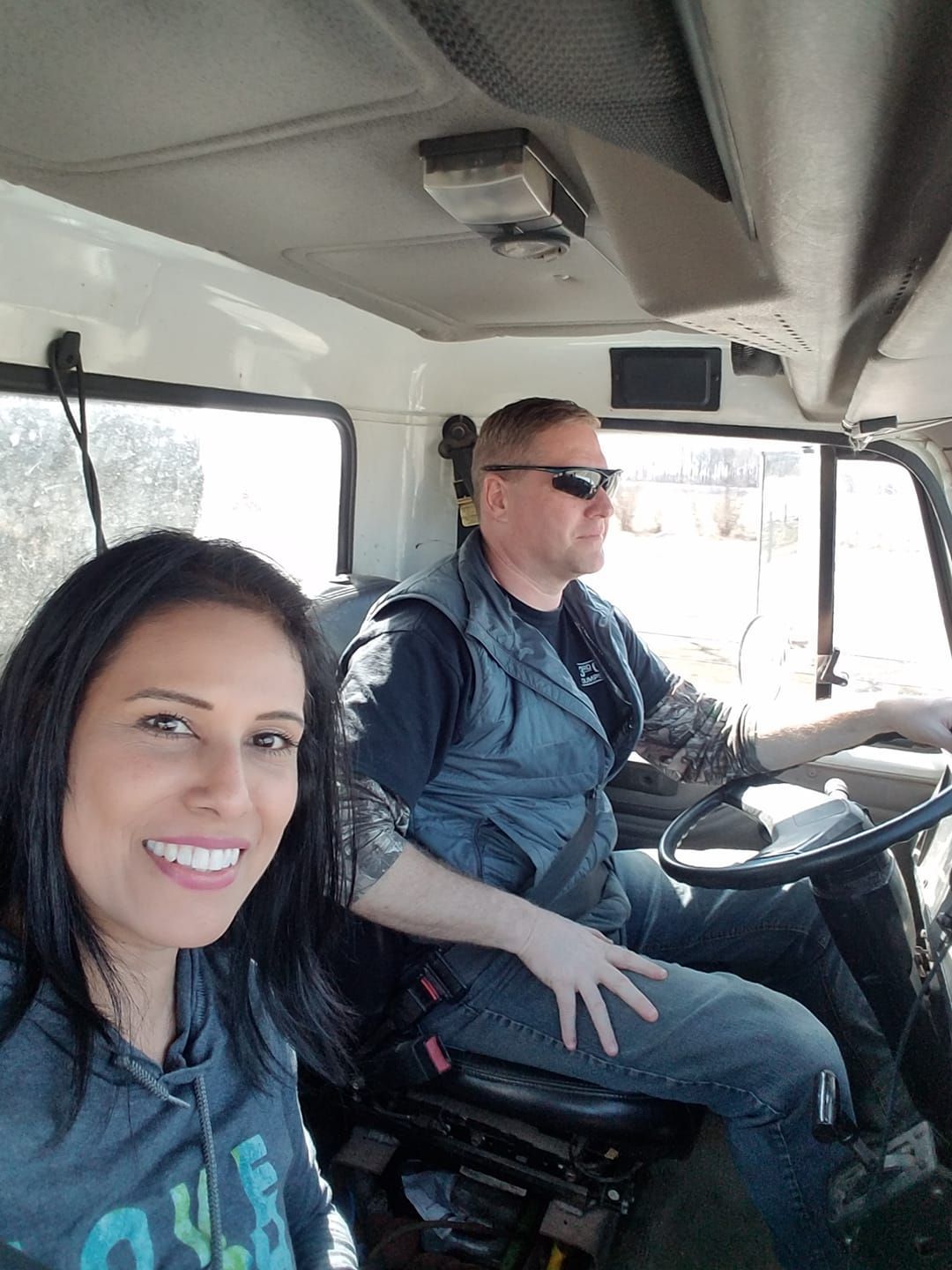 Woman and man in a truck cab; the woman smiles, the man drives while wearing sunglasses.