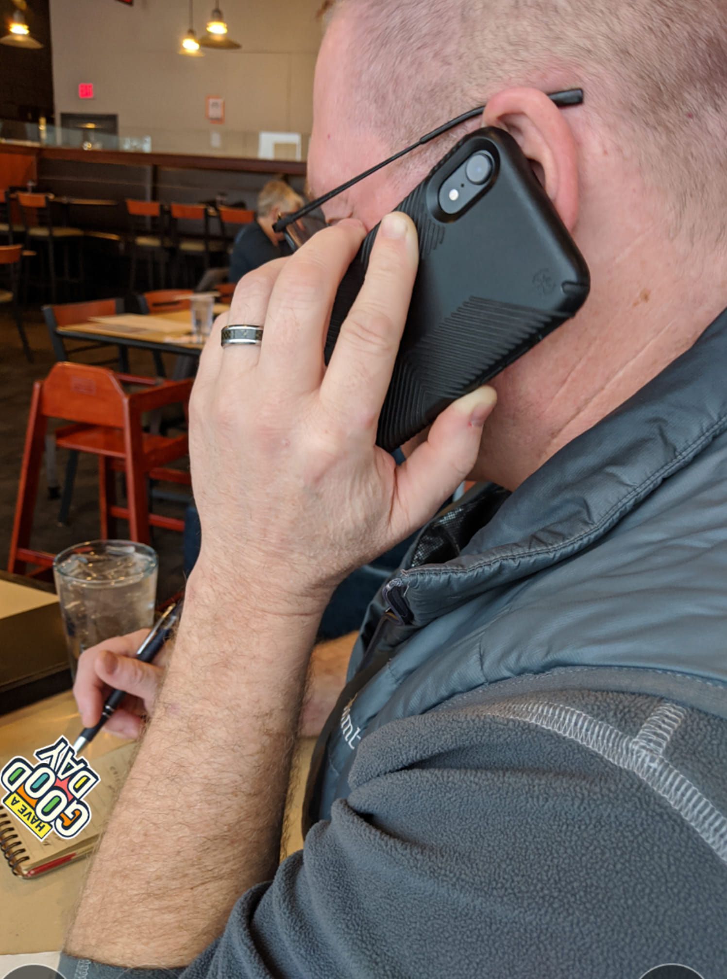 Person holding a phone to their ear, writing, sitting at a restaurant table.