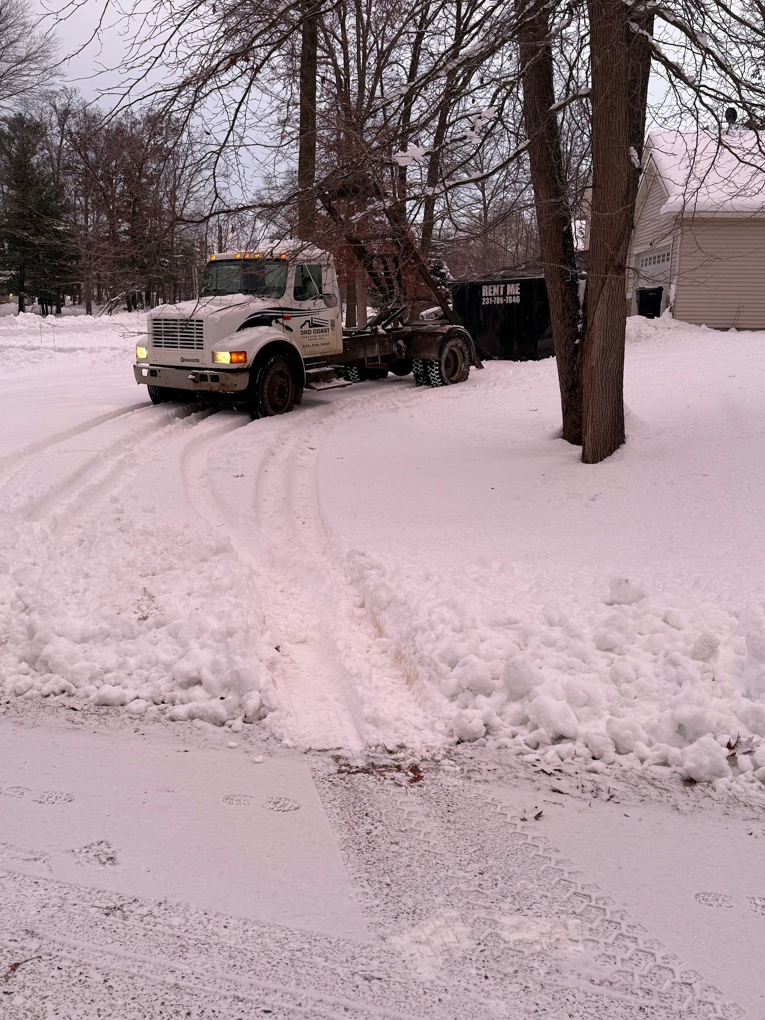 White truck pulling trailer in snowy driveway. Trees frame the scene.