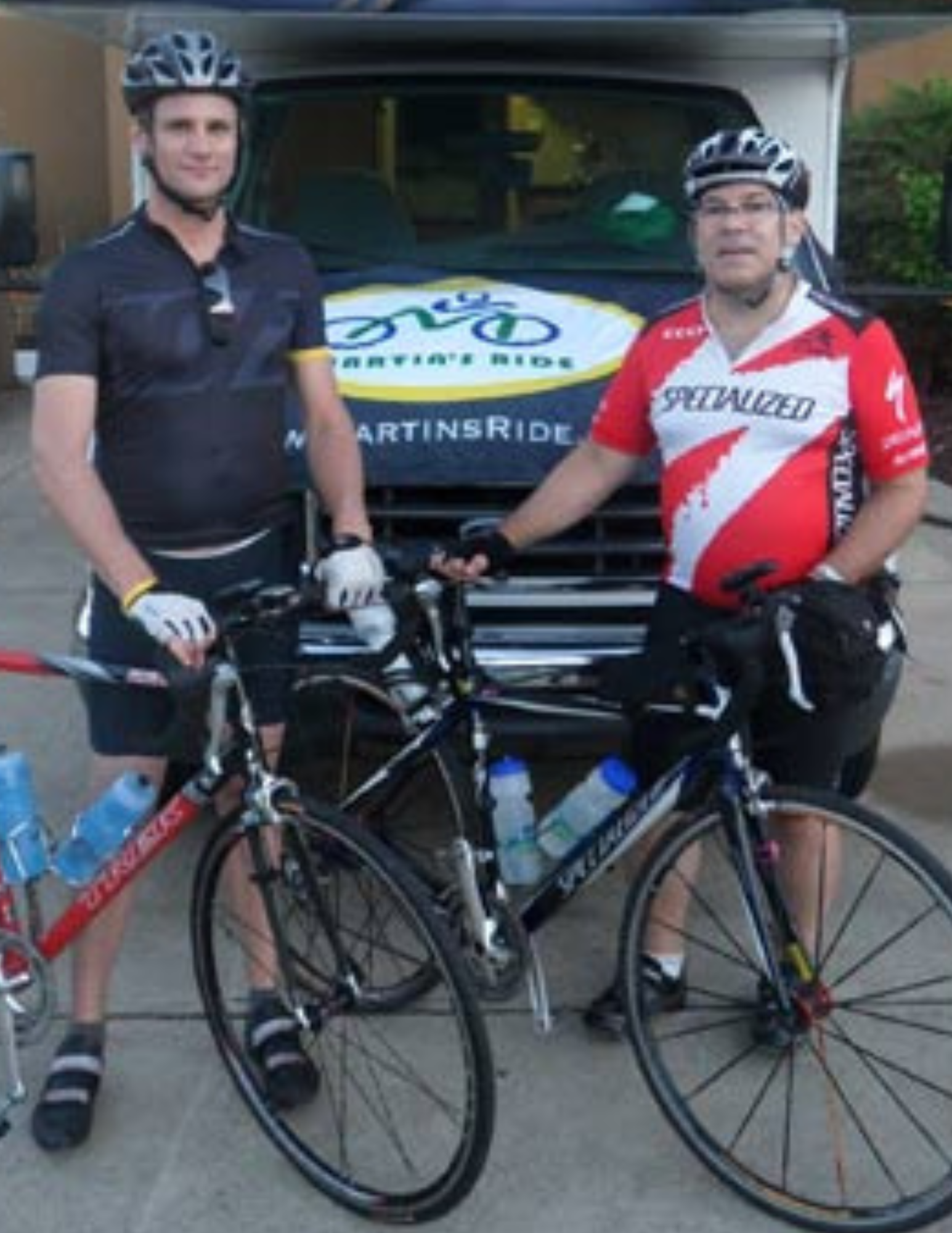 Two men standing next to bicycles in front of a van that says martin 's ride