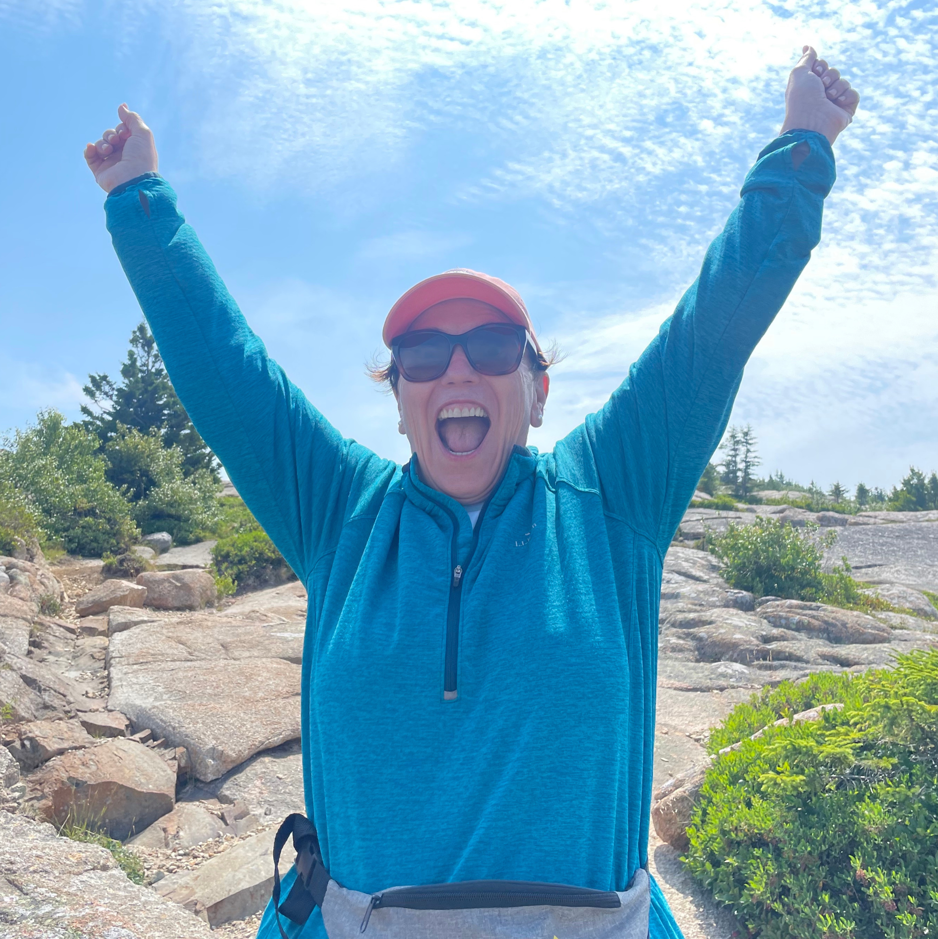 A woman wearing sunglasses and a hat is raising her arms in the air