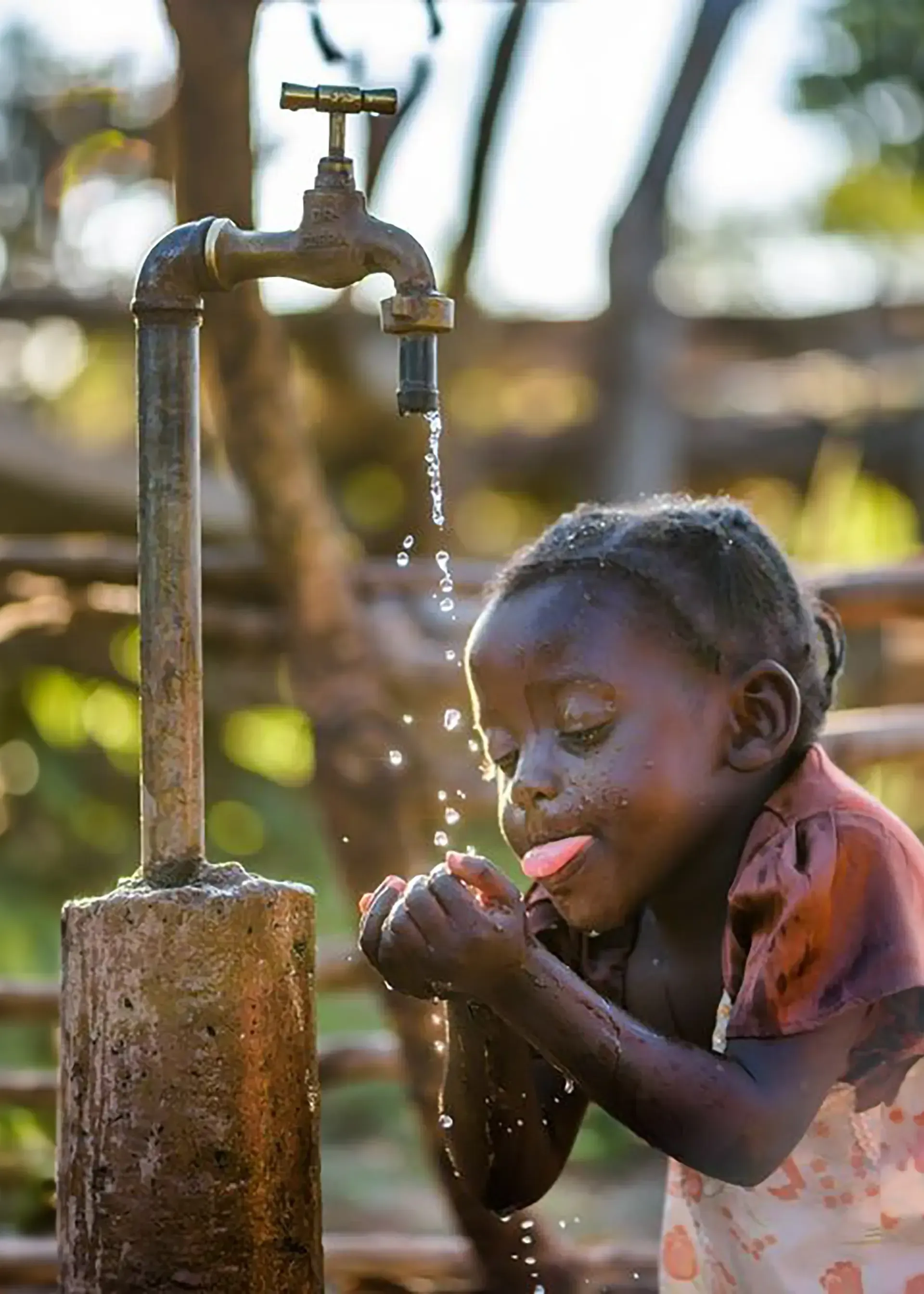 A little girl is drinking water from a faucet