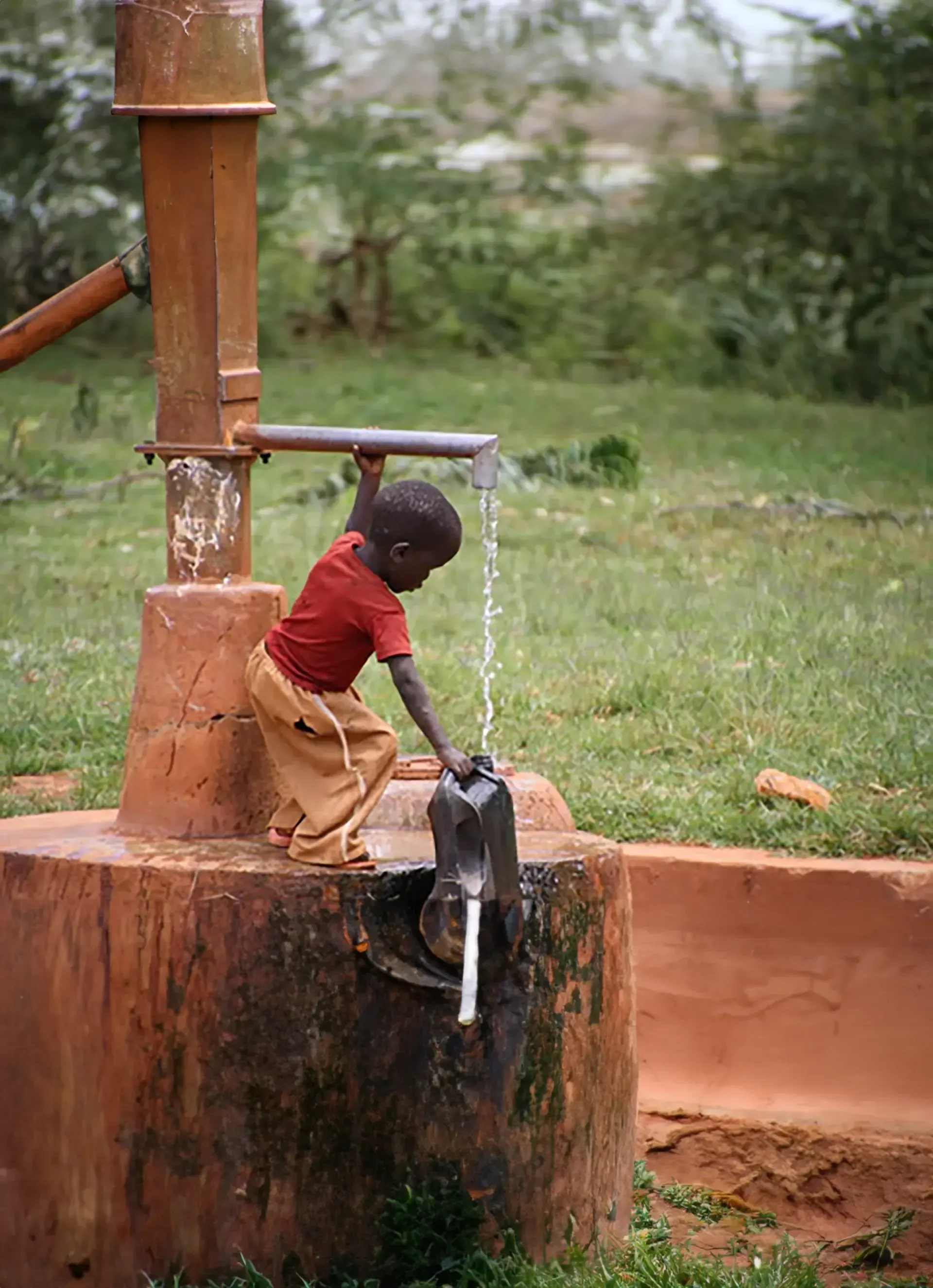 A young boy is drinking water from a well
