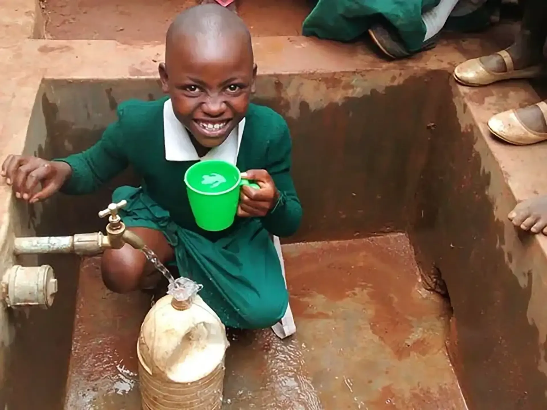 A young girl in a green school uniform is drinking from a green cup
