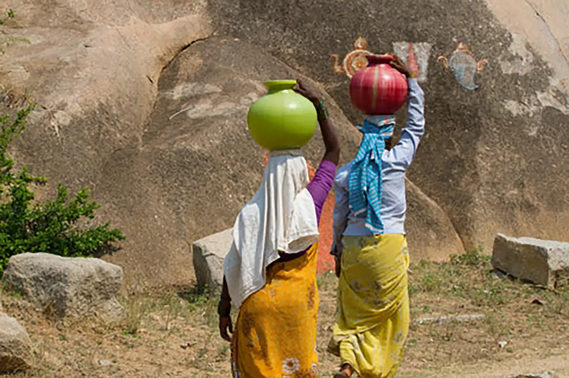 Two women are carrying large pots on their heads