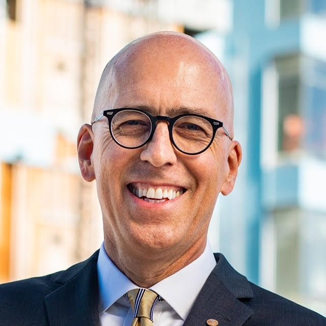 A bald man wearing glasses and a suit is smiling for the camera.