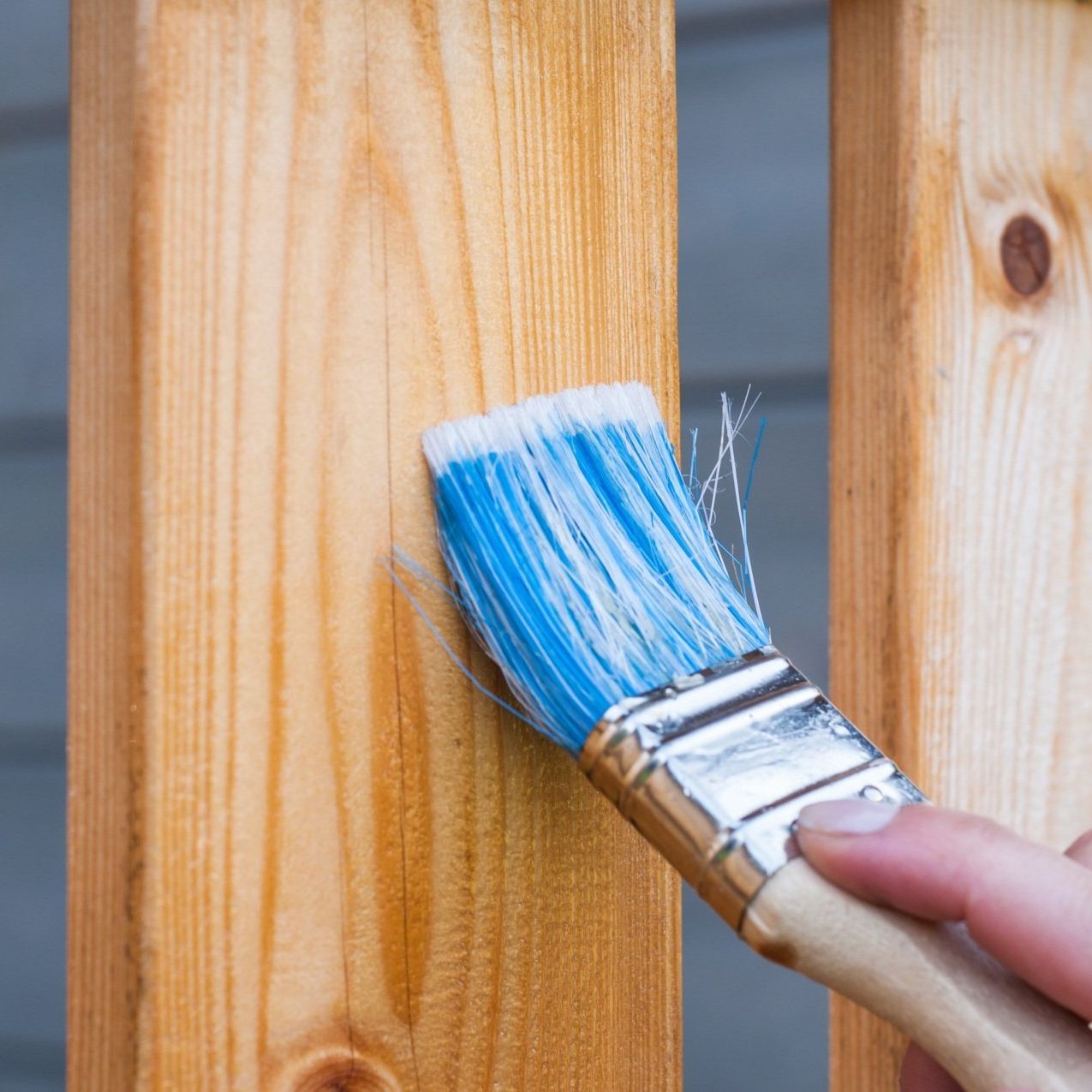 A person is painting a wooden railing with a blue brush.