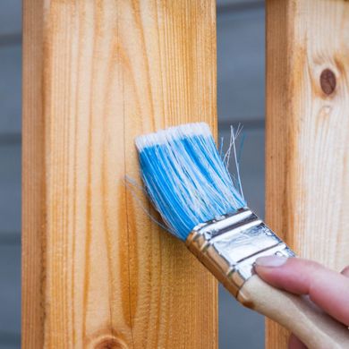 A person is painting a wooden railing with a blue brush.