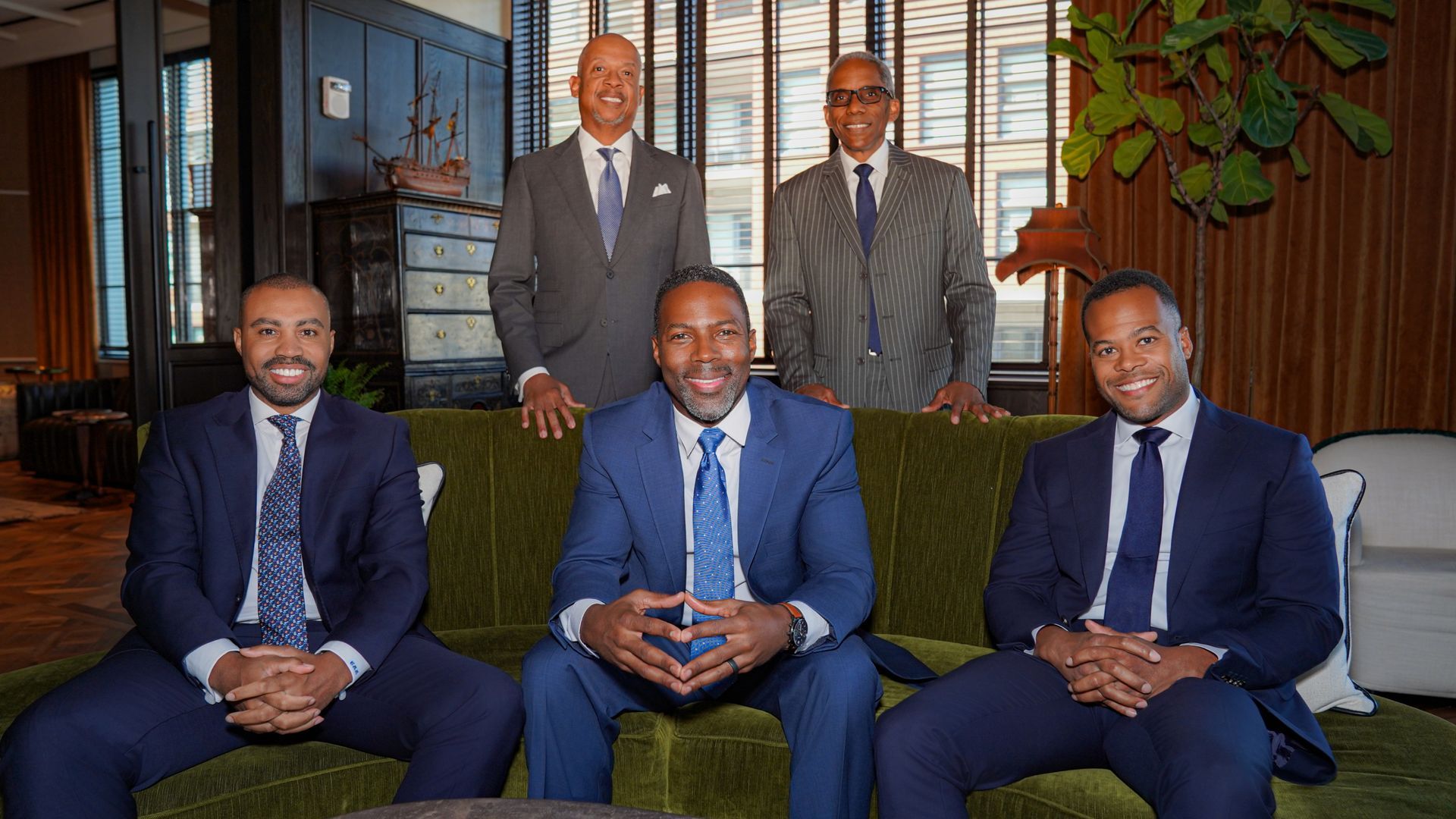 A man is sitting at a desk drinking coffee and talking on a cell phone.