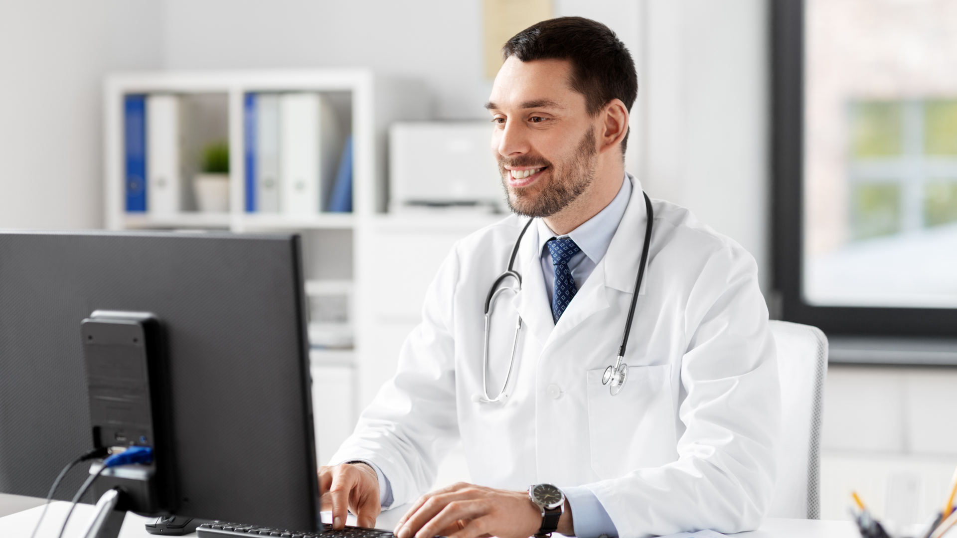 A doctor is sitting at a desk in front of a computer