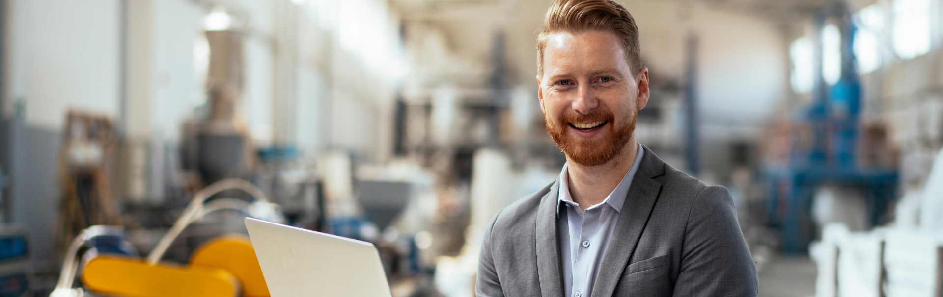 A man in a suit is holding a laptop computer in a factory