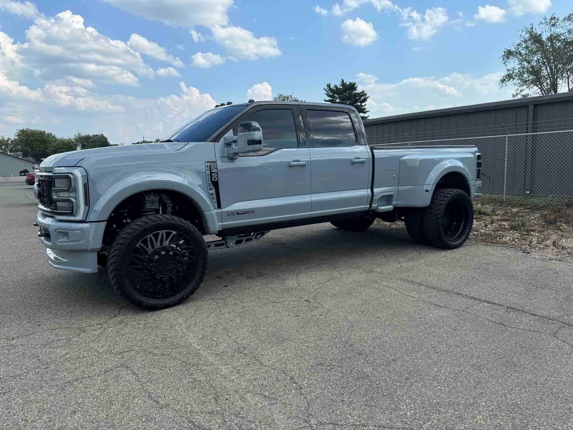 A gray truck is parked on the side of the road in front of a fence.