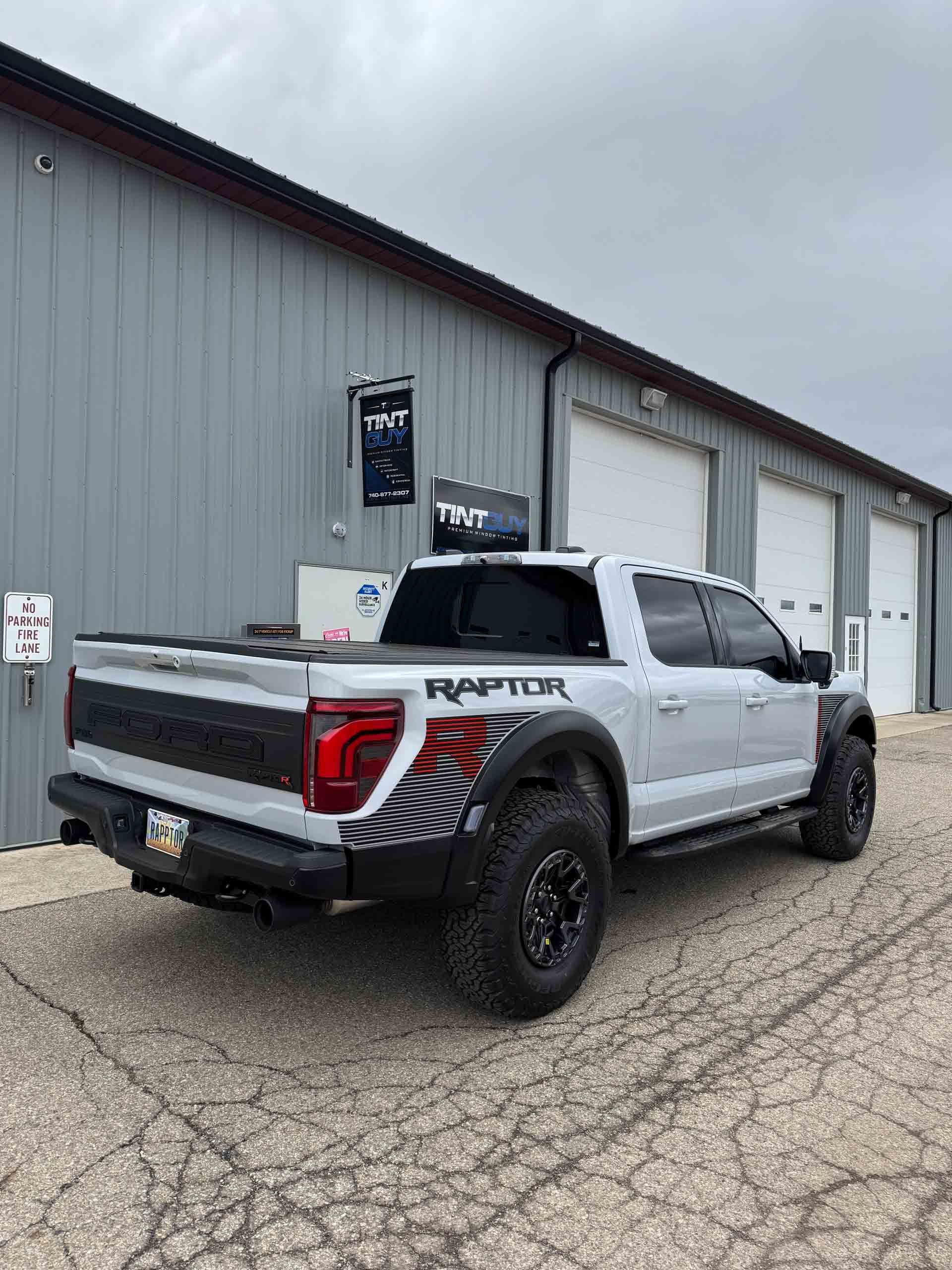 A white ford raptor truck is parked in front of a building.
